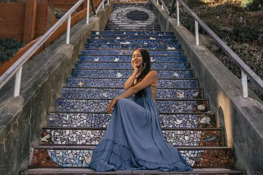 A woman poses sitting on the 16th Avenue tiled stairs in the Sunset neighborhood of San Francisco.