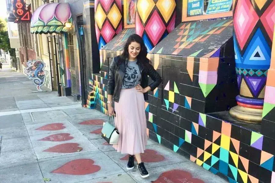 A woman stands on A sidewalk painted with red hearts, in front of a colorful storefront, in San Francisco's Haight-Ashbury neighborhd.