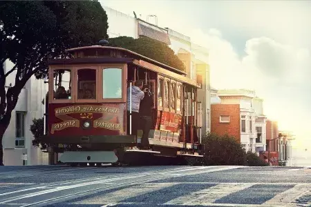 A cable car rounds A hill in San Francisco with passengers looking out the window.